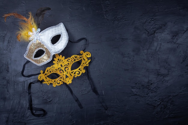 写真 2つのヴェネツィアのマスク1つは金色でもう1つは黒い背景に羽が付いている白いマスク