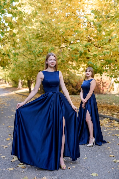 Two very beautiful young ladies in fashionable blue dresses in autumn park.