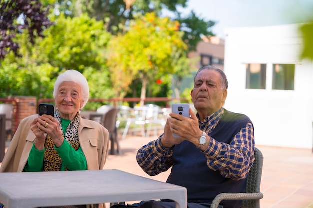 Two very happy elderly people in the garden of a nursing home looking at the phone technologies in the elderly