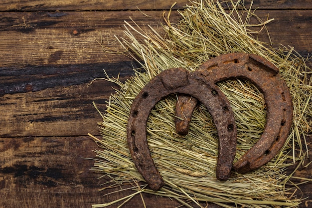 干し草に2つの非常に古い鋳鉄製の金属製の馬の蹄鉄。幸運のシンボル、聖パトリックの日の概念。アンティークの木製の背景