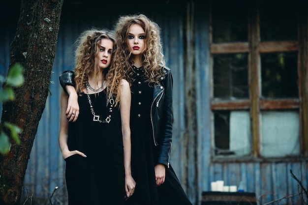 Two vintage women as witches, posing beside an abandoned building on the eve of Halloween