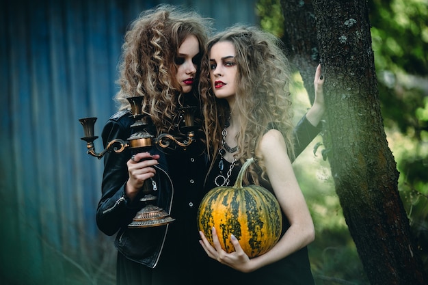 Photo two vintage women as witches, posing in front of an abandoned house on the eve of halloween