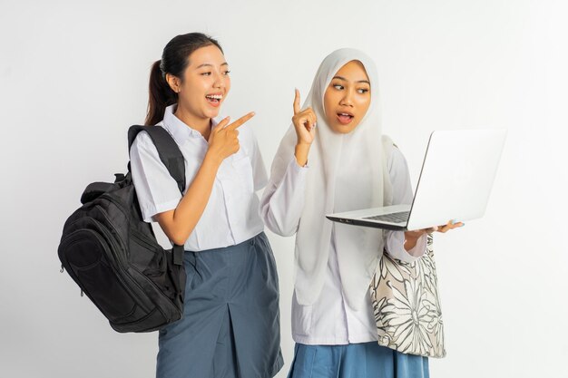 Two vocational high school girls jokingly carrying bags while using a laptop on a white background