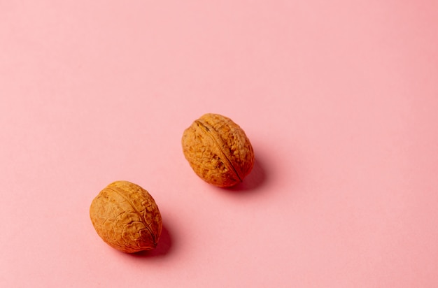 Two walnuts on a pink surface