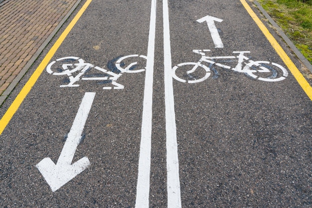 Pista ciclabile a doppio senso con segni di bicicletta e frecce dipinte su asfalto.