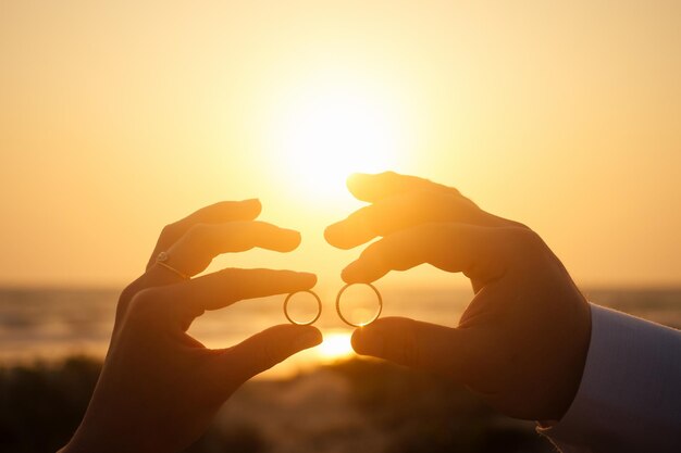 夕暮れ時の海辺の前の珊瑚に2つの結婚指輪