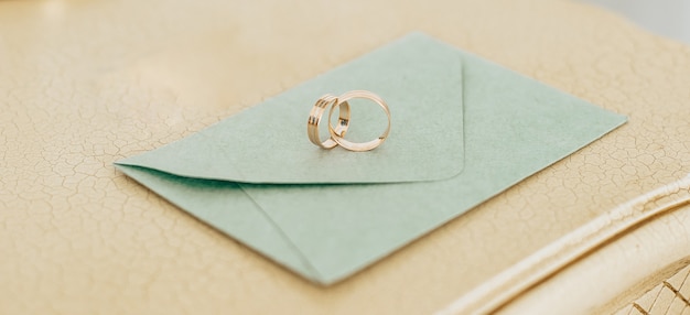 Two wedding rings lie on an invitation with gold background