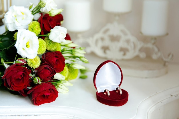 Two wedding rings in white and red gold with a bridal bouquet with red roses