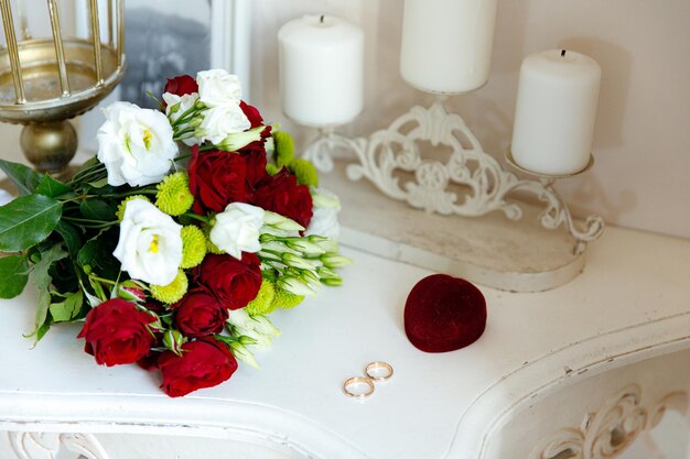 Two wedding rings in white and red gold with a bridal bouquet with red roses