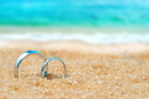 Two wedding silver rings in the sand on the background of beach and sea