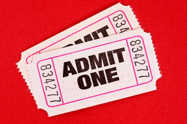 Two white admit one movie tickets on red.