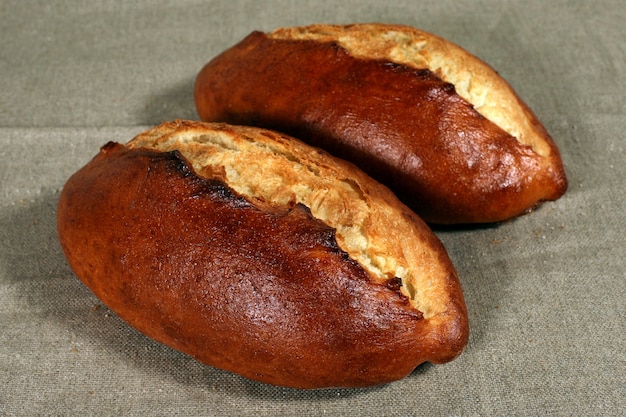 Два белых хлеба лежат на серой льняной скатерти
