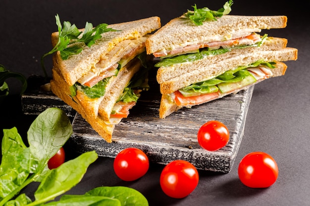 two white bread sandwiches lie nearby, next to lettuce, cherry tomatoes, on a black vintage cutting