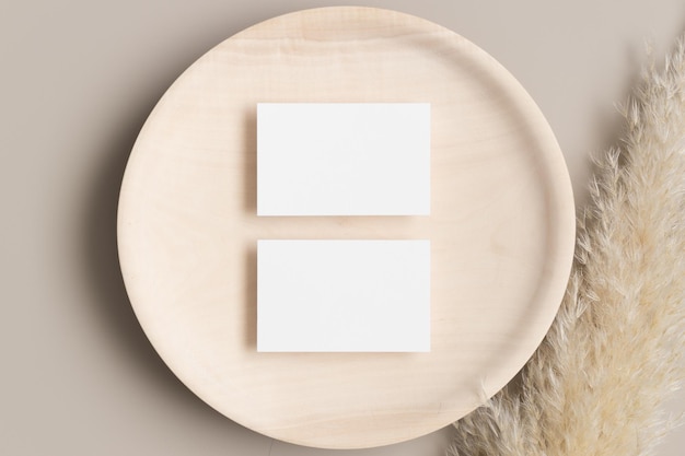 Two white business cards mockup 85x55mm on a wooden plate with a pampas grass decoration