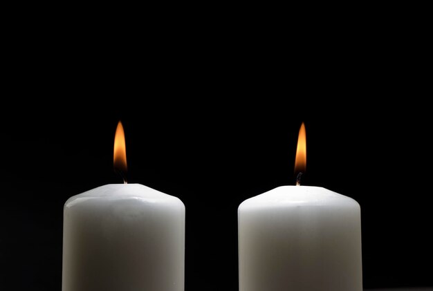 Two white candles with the flame of the flame on the left side.