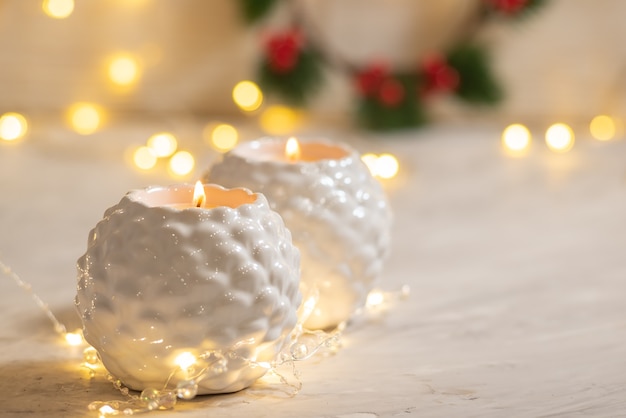 Two white candlesticks with burning canles flame with garland lights