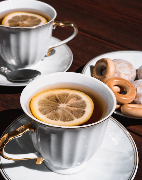 Две белые чашки черного чая с лимоном на деревянном столе и вкусные рогалики и пряники