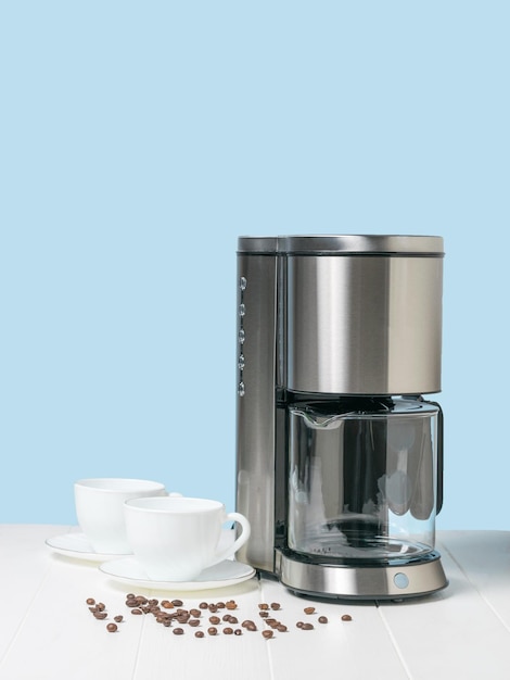 Two white cups and a coffee maker with coffee beans on a white table