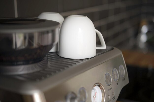 검은 타일 벽에 붙어 있는 세련된 회색 커피 머신에 흰색 컵 2개