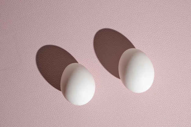 Two white eggs on a pink background in hard light.