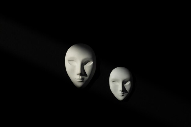 Two white gypsum mask of human with closed eyes on black background