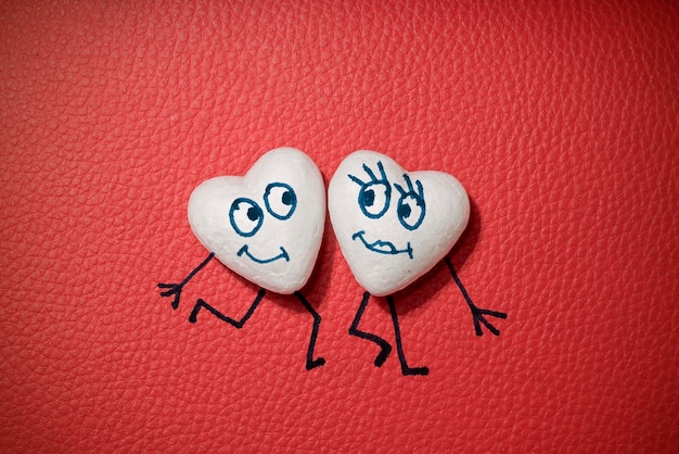 Two white hearts with happy faces on red leather background