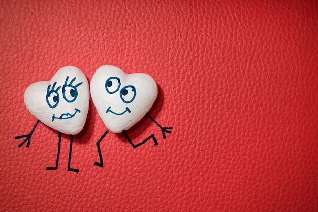 Two white hearts with happy faces on red leather background