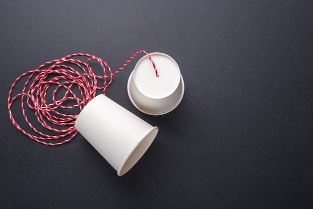 Two white paper cup connect with red rope used for classic phone