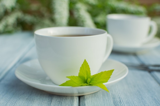 Фото Две белые фарфоровые чашки с чаем на деревянном столе на фоне белых цветов