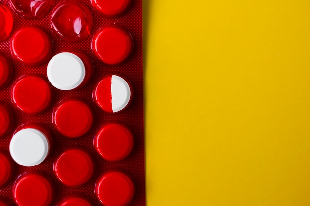 Две белые круглые таблетки с половиной на красной упаковке на желтом