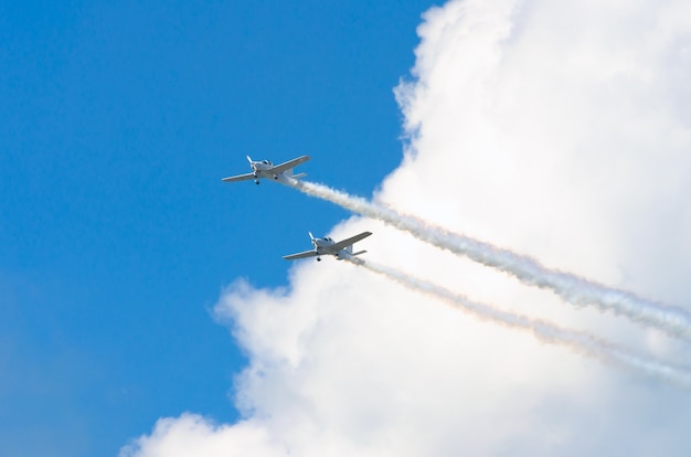 Two white turboprop airplane with a trace of white smoke against a blue sky.