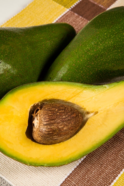 Two whole avocados and a avocado cut in a half over a white surface.