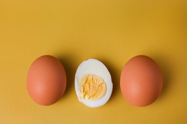写真 孤立した薄黄色の背景に卵黄を半分に切った2つの丸ごとの茶色の卵とゆで卵