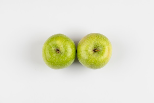 Two whole green apples isolated on a white table. 