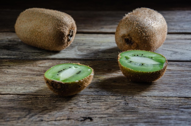 Two whole kiwi fruits and one cut on a kitchen wooden table.