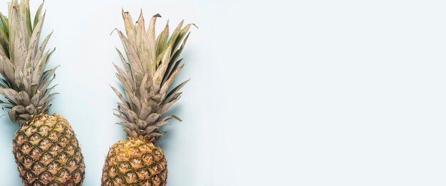 Two whole ripe pineapple and the shadow of palm leaves on a light background