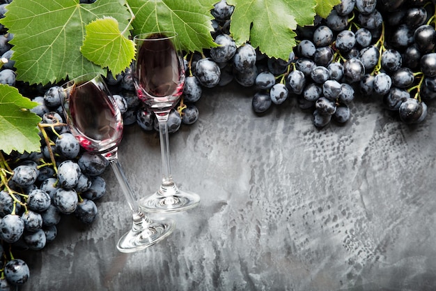 Due bicchieri di vino pieni di vino che giace in cornice fatta di uva. uva succosa nera vino rosso su fondo di cemento scuro vintage. copia spazio su sfondo nero scrostato. confine.