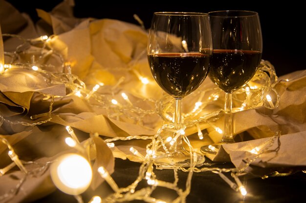 two wine glasses stand in a shining yellow garland on craft paper. cozy romantic celebration...