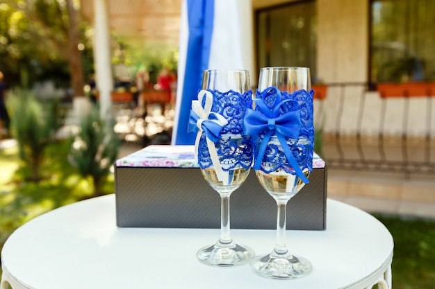 Two wineglasses with blue ribbon and gift box on a table on wedding ceremony