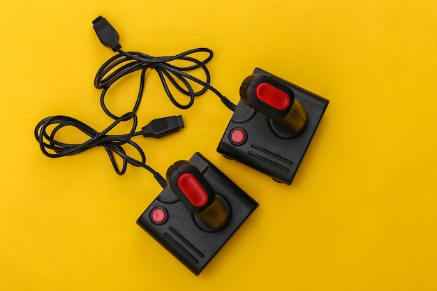 Two wired retro joysticks with wound cable on yellow background. video game, gaming. top view