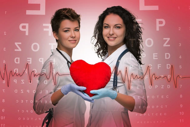 Two woman doctor holding a red heart on red ophthalmic table background