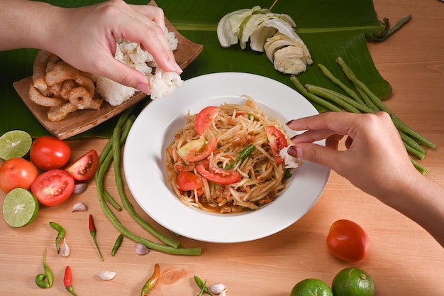 Two woman eating sticky rice with green papaya salad by their hand