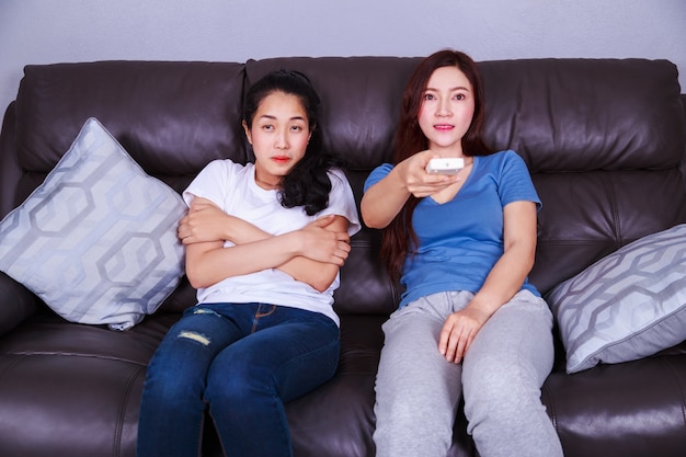 two woman hand hold remote air conditioner on sofa at home