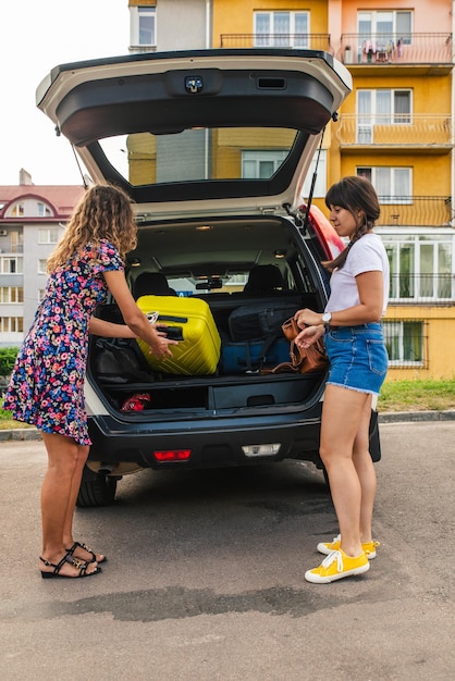 Photo two woman packing luggage in car trunk. road trip