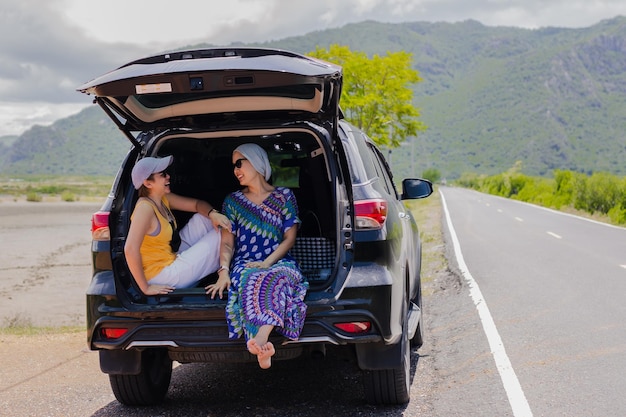 Two woman sitting at the car trunk on a road trip