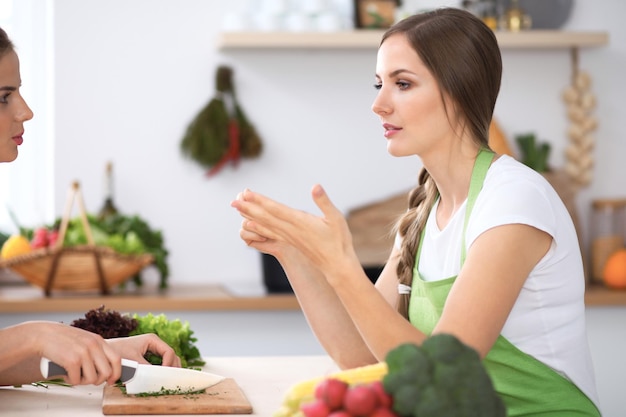 Due donne stanno cucinando insalata fresca in una cucina e si divertono a parlare con gli amici e il concetto di chef cook