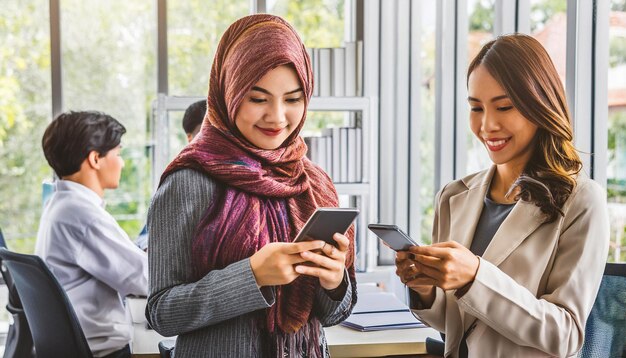 Photo two women are looking at their phones and one is holding a phone