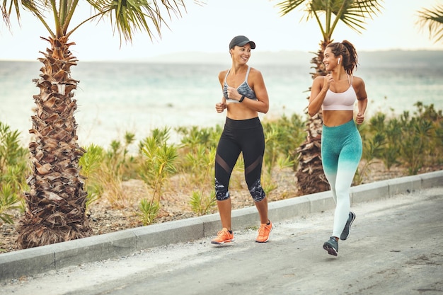 Two women are running along the path of a Mediterranean town by the sea and enjoying in summer sunny day.