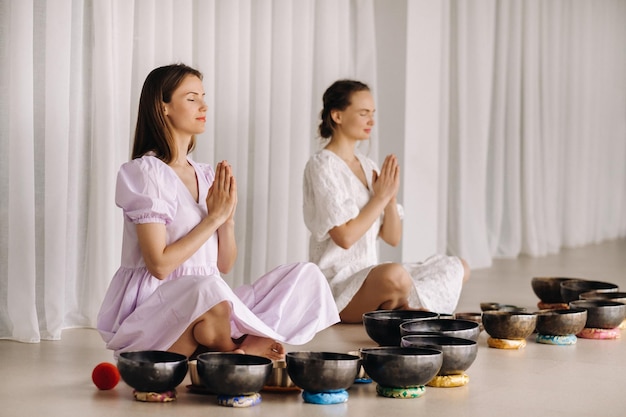 two women are sitting with tibetan bowls in the lotus position before a yoga class in the gym
