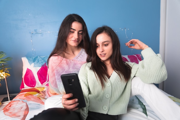 Two women on a bed using a smartphone